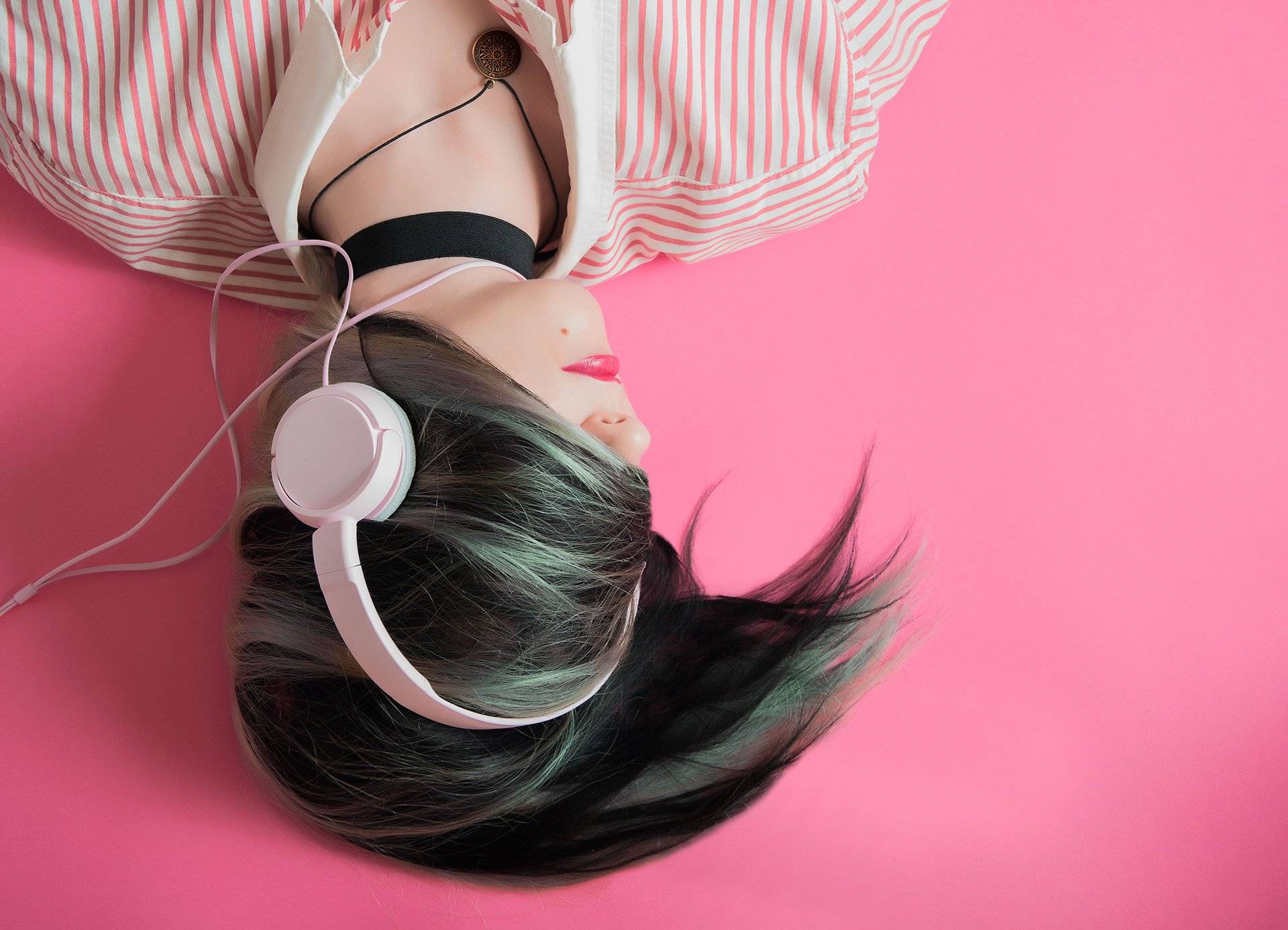 Trendy girl upside down with headphones on a pink background – expressing fashion through music