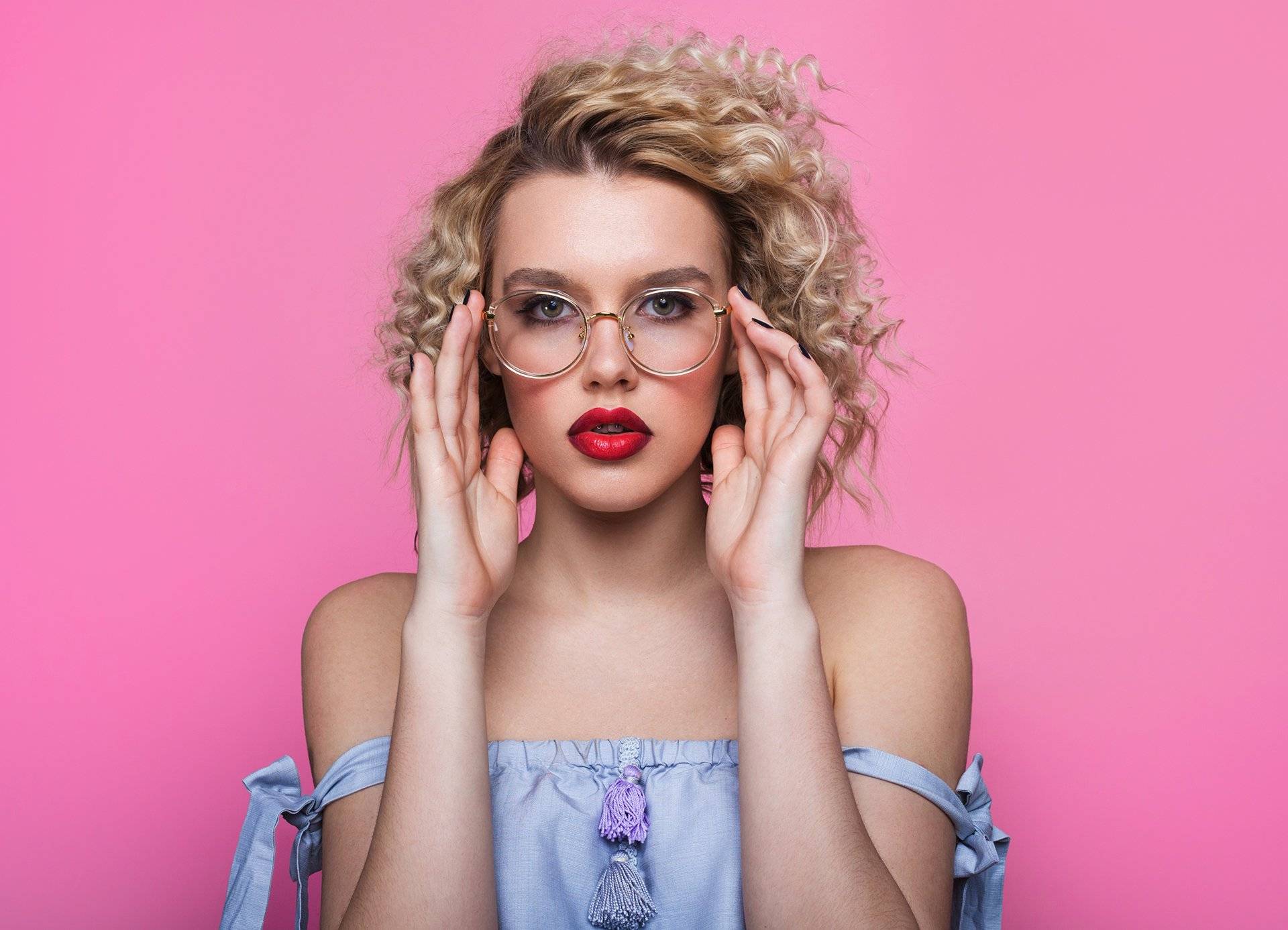 Curly blonde fashionista with red glasses and shocked expression against a pink background