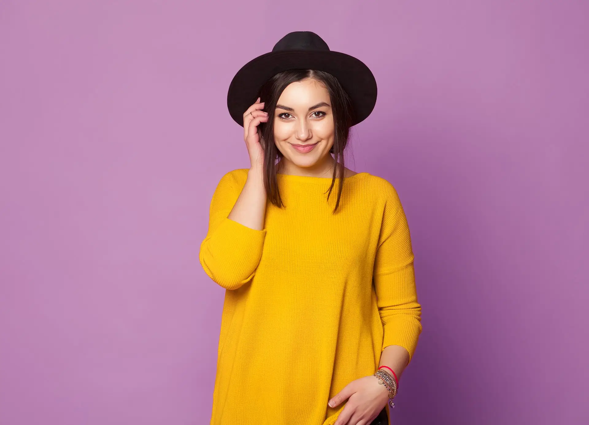 Girl in mustard yellow dress and black hat posing sweetly against a pastel lilac background